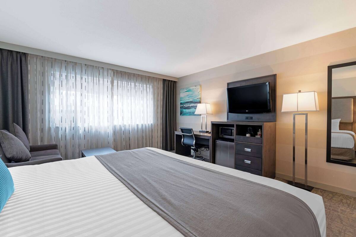 Habitación de hotel con una cama grande, un escritorio con silla, un televisor de pantalla plana, una lámpara de escritorio y un espejo.