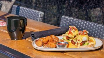 Un plato de comida que incluye huevos Benedictinos, una taza pequeña y una servilleta sobre una mesa de madera.