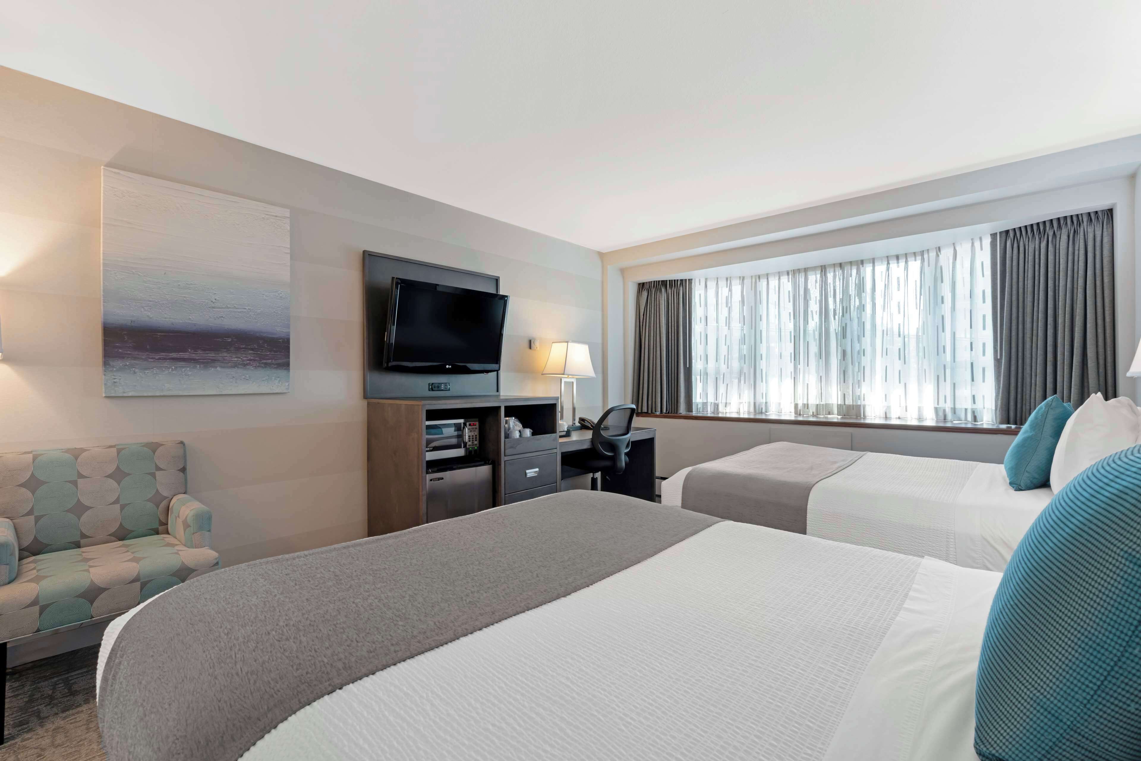 A hotel room with two beds, a desk with a computer, a TV, and a window with curtains.