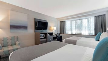 A hotel room with two beds, a desk with a computer, a TV, and a window with curtains.