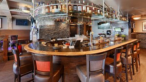 Een bar met een gebogen toonbank, diverse zitplaatsen en een ruime keuze aan flessen en glazen.