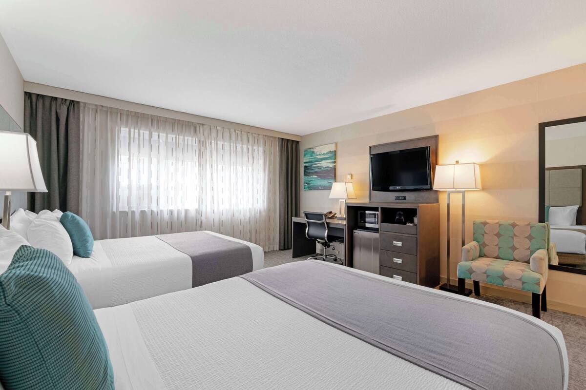 Habitación de hotel con dos camas, un escritorio, un televisor y una silla.