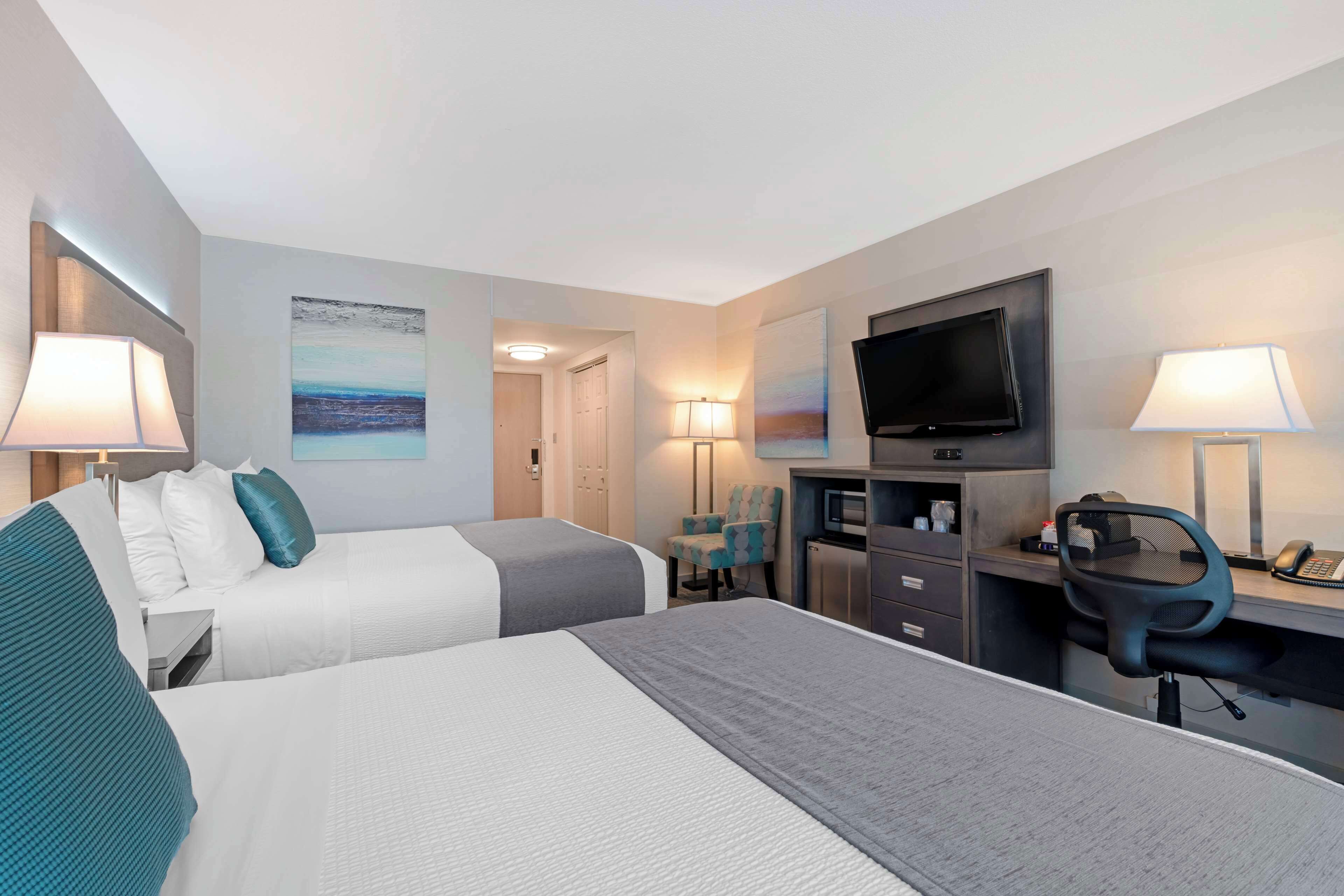A hotel room with two beds, a desk with a chair, a television, and a desk lamp.