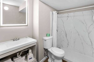 Un baño con lavamanos blanco, espejo, inodoro y pared de ducha de mármol.