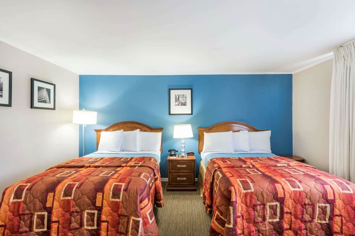 Une chambre d’hôtel avec deux lits, un mur d’accent bleu, des tableaux encadrés, des lampes de chevet et un téléphone sur la table de chevet.