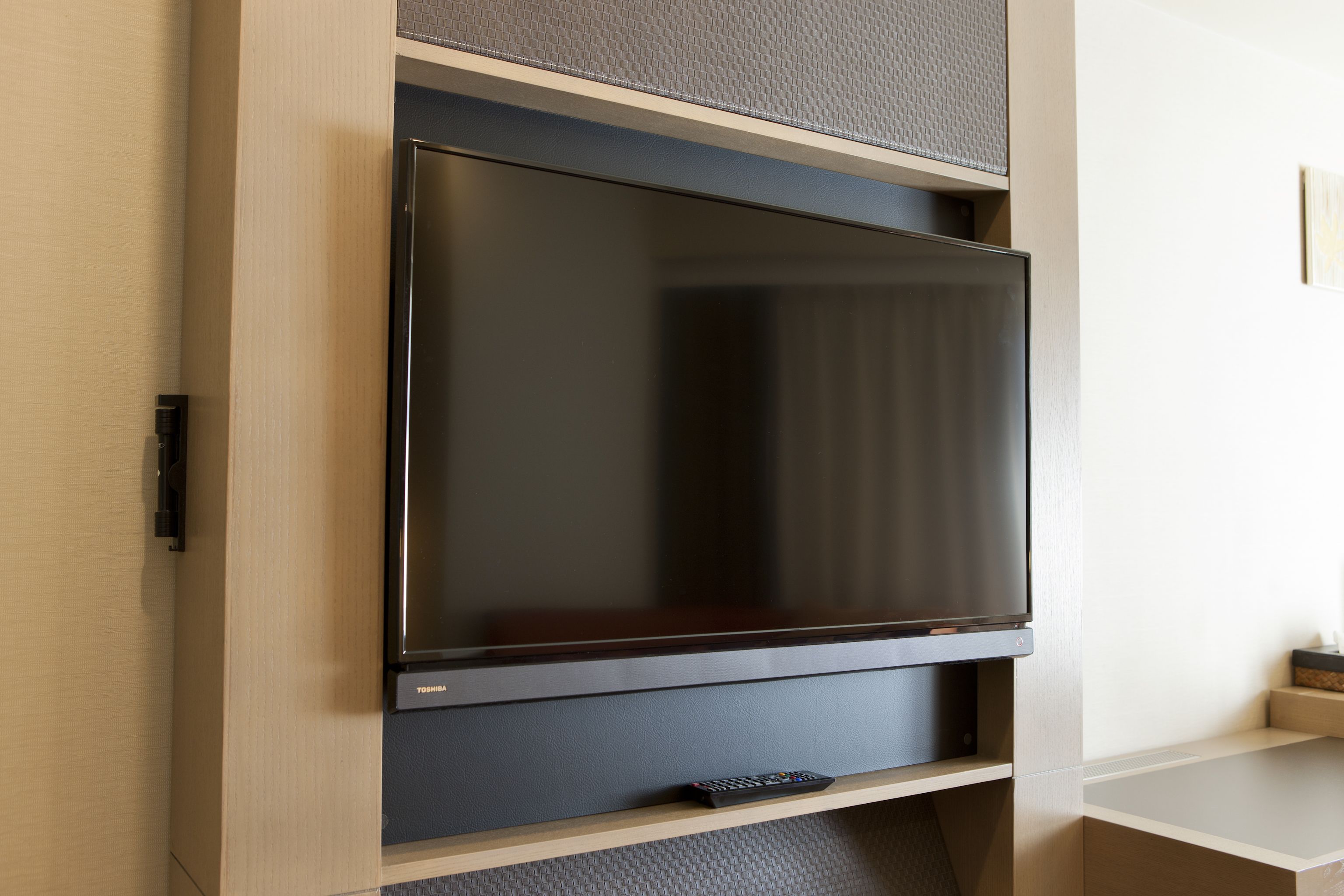 A flat-screen TV mounted on a wooden wall with a remote control on a shelf below.