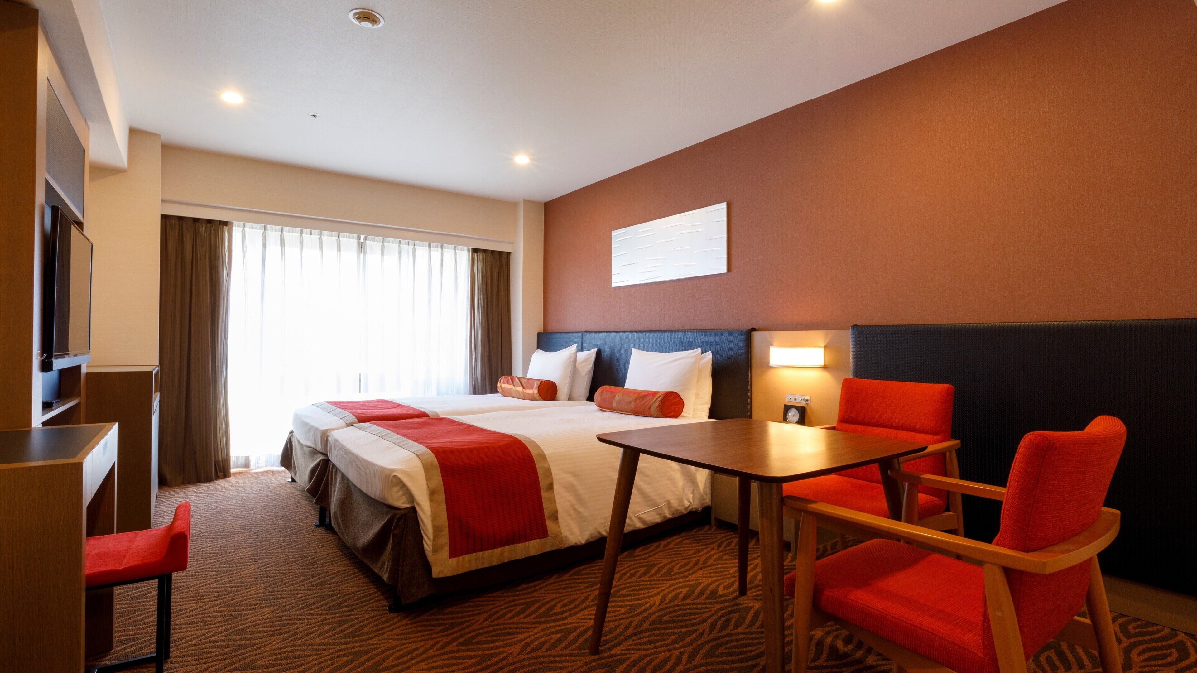 A hotel room with a bed, two red chairs, a desk, and a television.