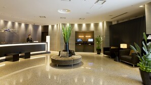 Un hall d’hôtel moderne avec un comptoir d’accueil, un espace salon et une grande plante en pot.