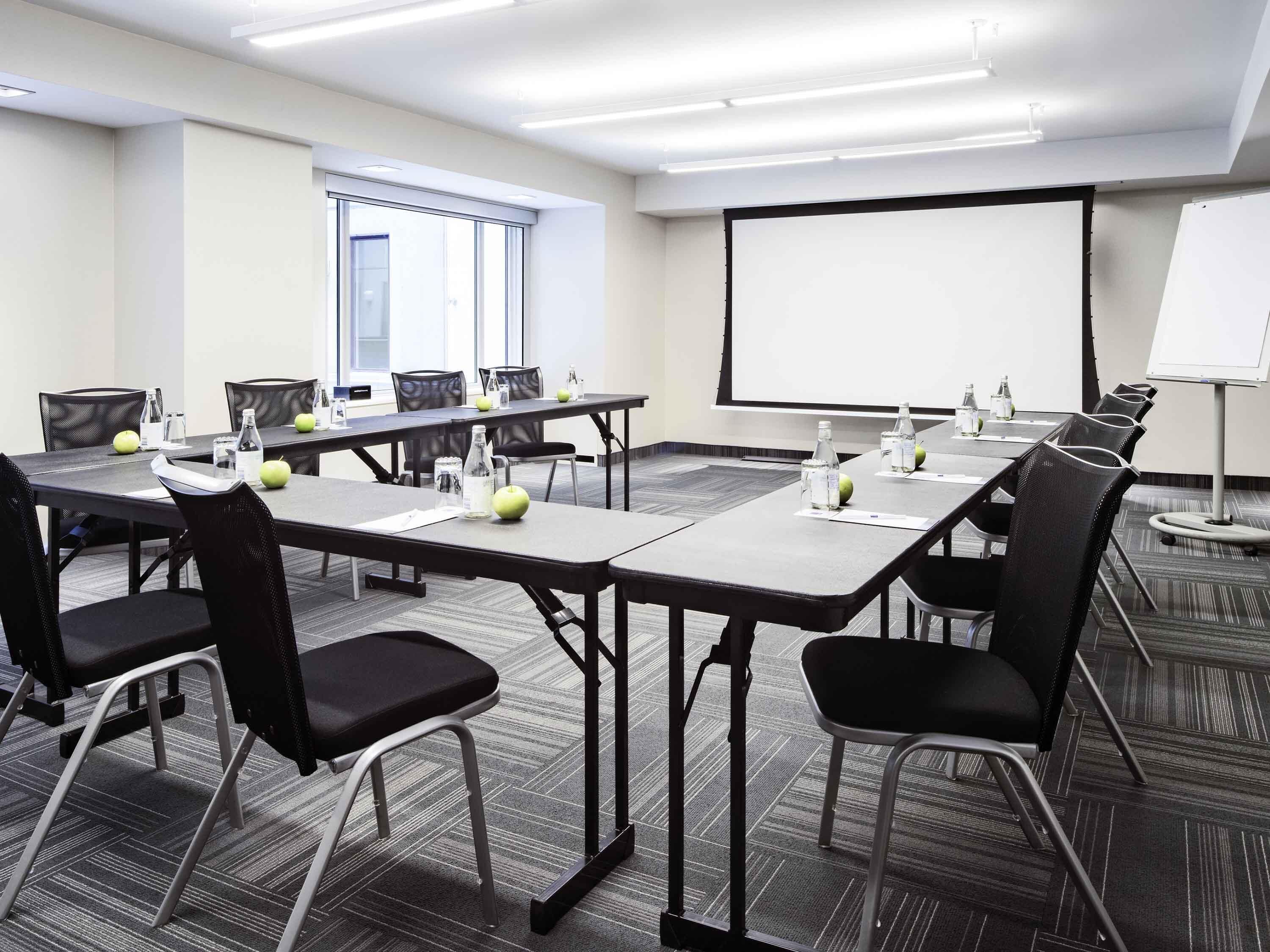 A conference room with a whiteboard, projector screen, and multiple tables with chairs.