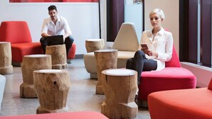 A modern lounge area with red and beige seating, wooden stools, and a glass wall with natural light. - Novotel Montreal Centre (Montreal)