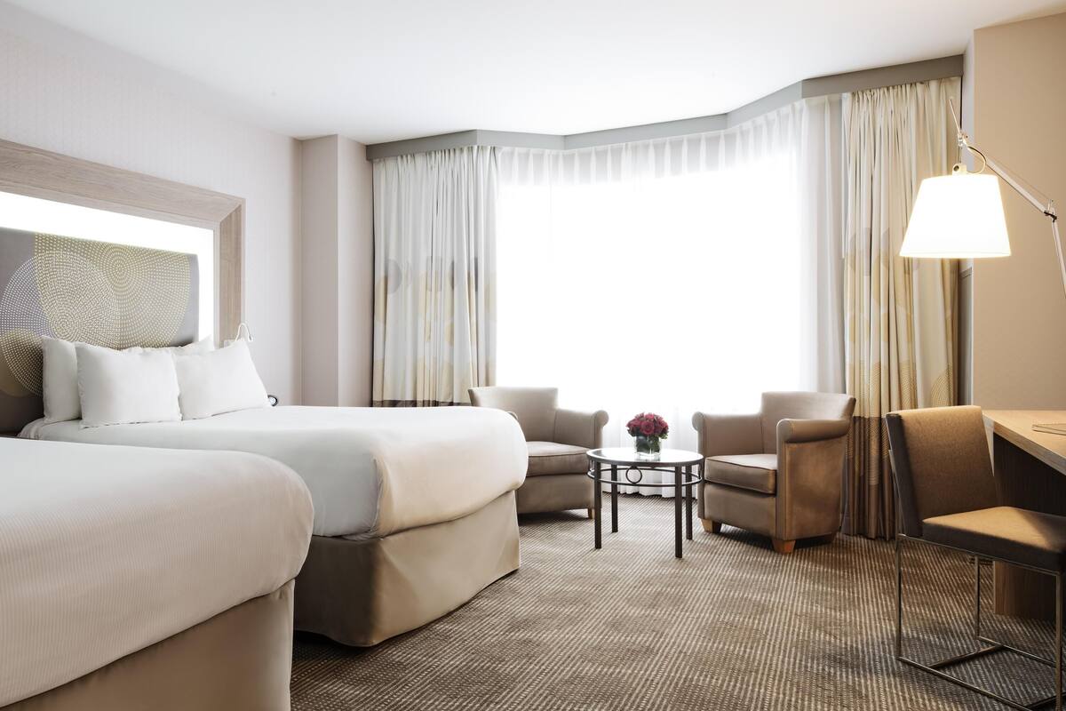 Une chambre d’hôtel avec un lit, deux fauteuils, une petite table et un bureau.