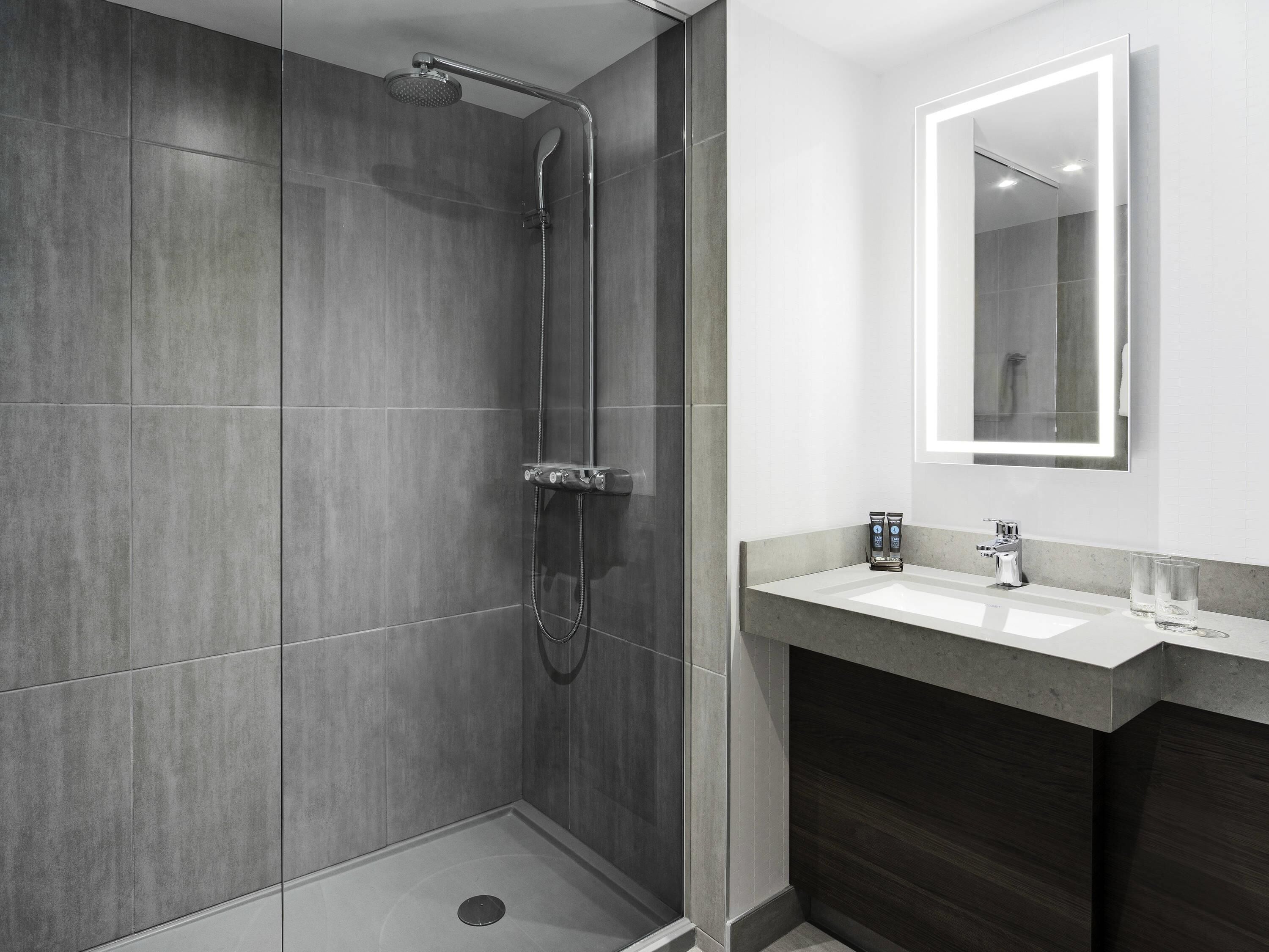 Eine moderne Dusche mit Glastür, ein Waschtisch mit Spiegel und ein Waschbecken.