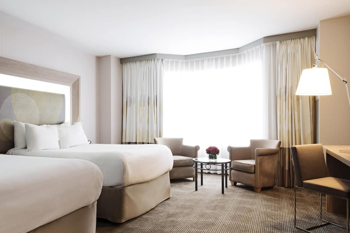 A hotel room with a large bed, two armchairs, a small table, and a desk.