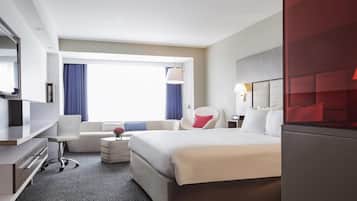 Une chambre d’hôtel avec un lit, un bureau, une chaise, une petite table et une fenêtre avec des rideaux.