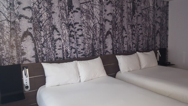 Habitación de hotel con dos camas, cabecera con panel de control y pared con diseño de árbol.