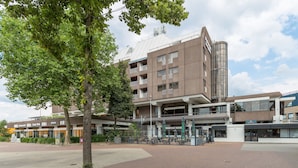 A modern building with multiple floors, outdoor seating, and a tree in the foreground. - Leonardo Hotel Lelystad City Center (Lelystad)
