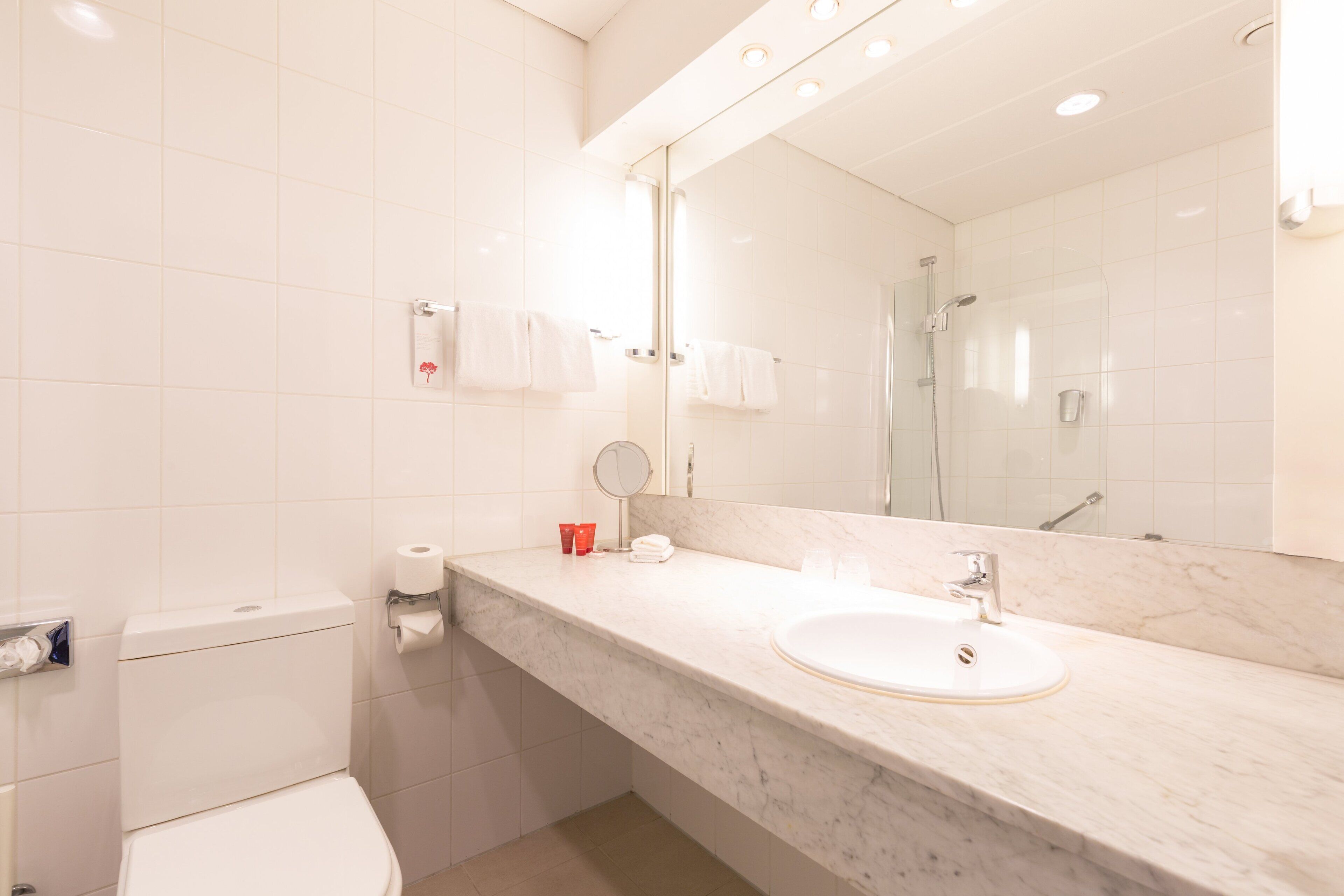 Un baño moderno con inodoro blanco, lavamanos y un espejo grande.