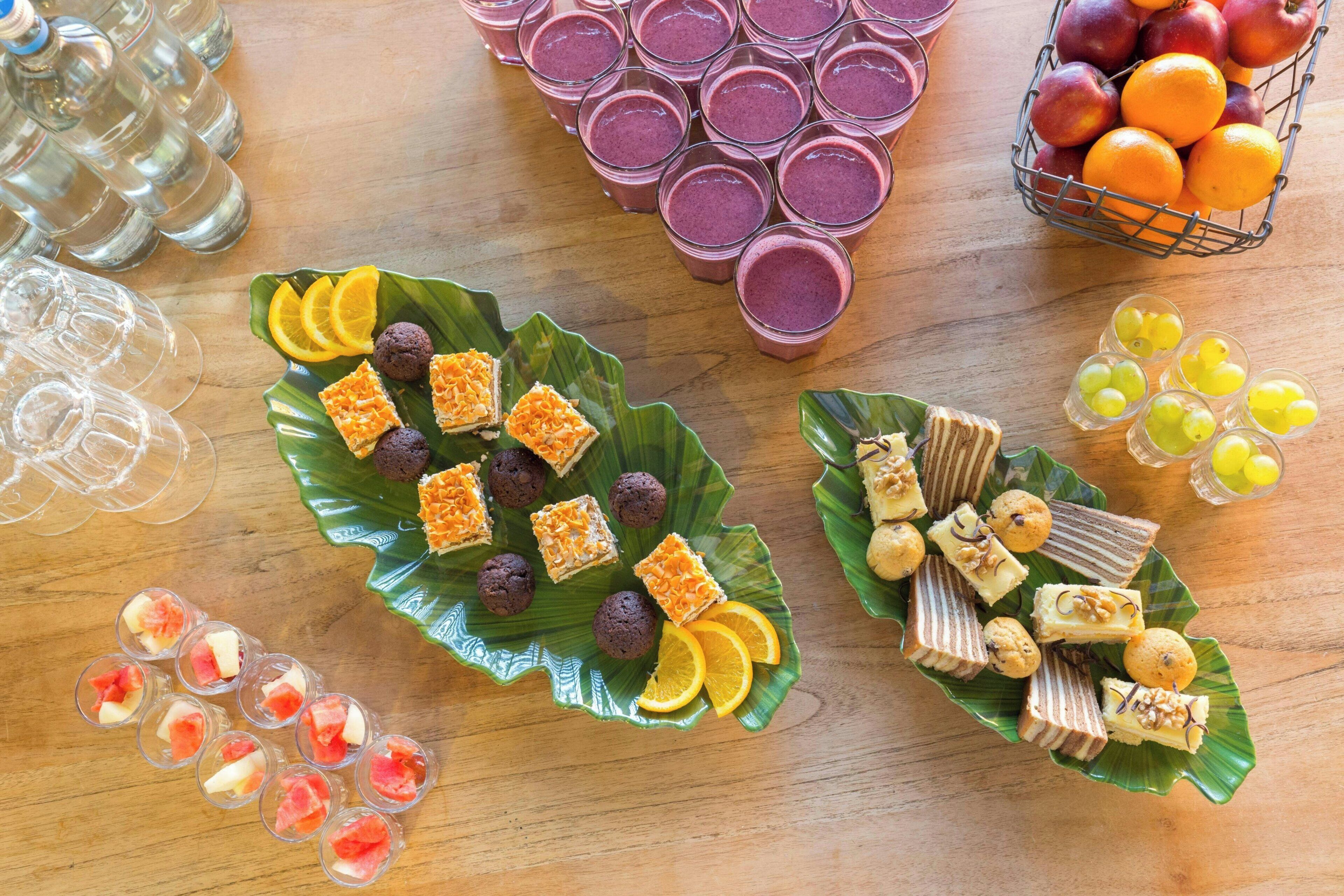 A table with various food items and drinks, including glasses of juice, a basket of oranges, and plates of desserts.