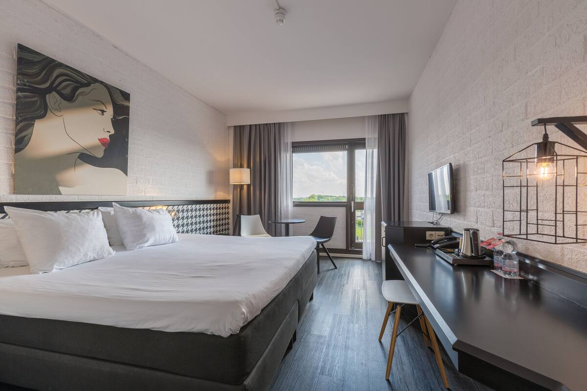 Een hotelkamer met een groot bed, een bureau met een lamp, een televisie en een schilderij aan de muur.