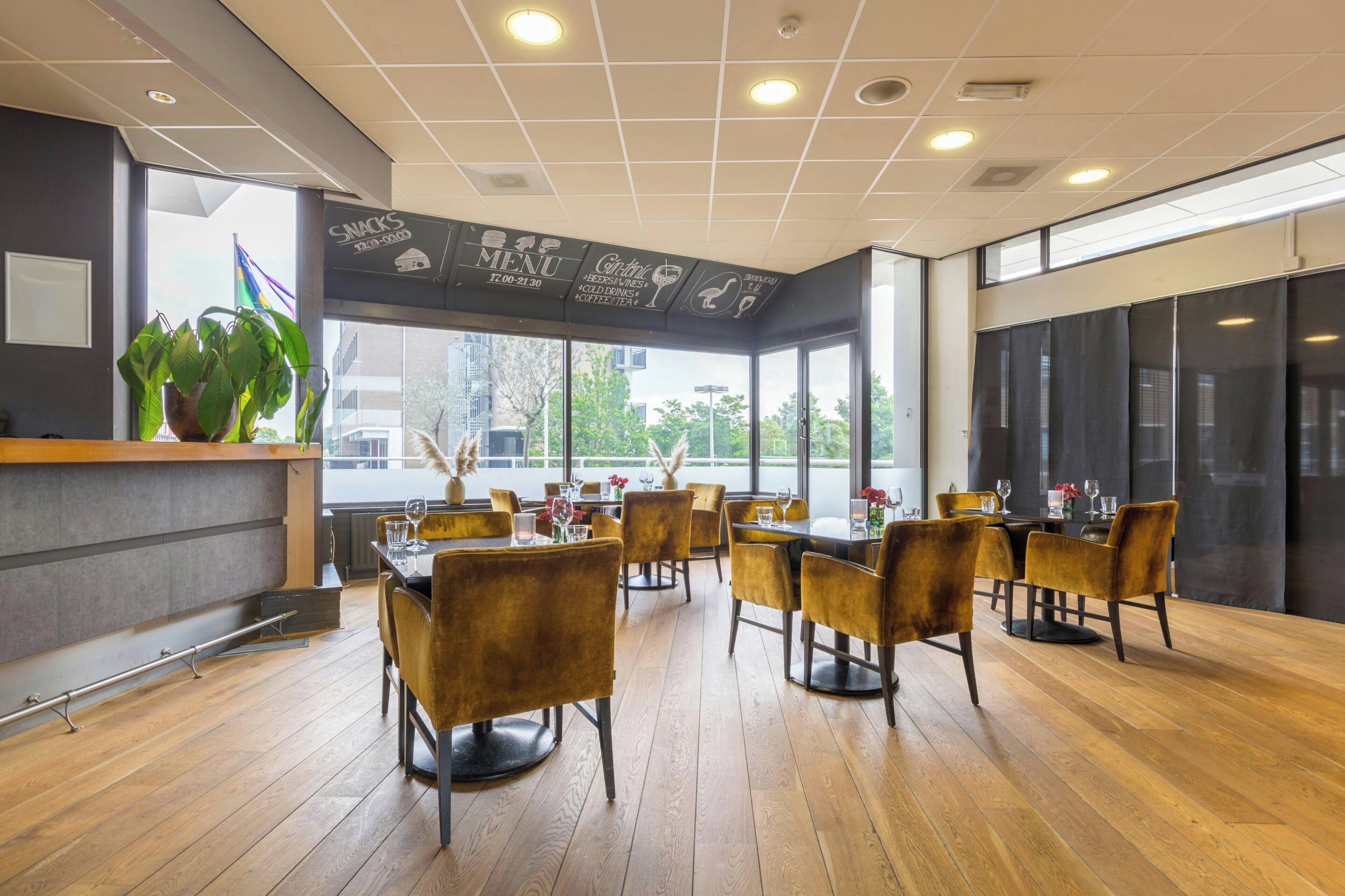 A restaurant interior with wooden flooring, brown chairs, a menu board, and large windows.
