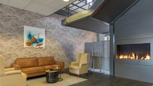 A modern interior with a brick wall, a fireplace, a sofa, and two armchairs. - Leonardo Hotel Lelystad City Center (Lelystad)