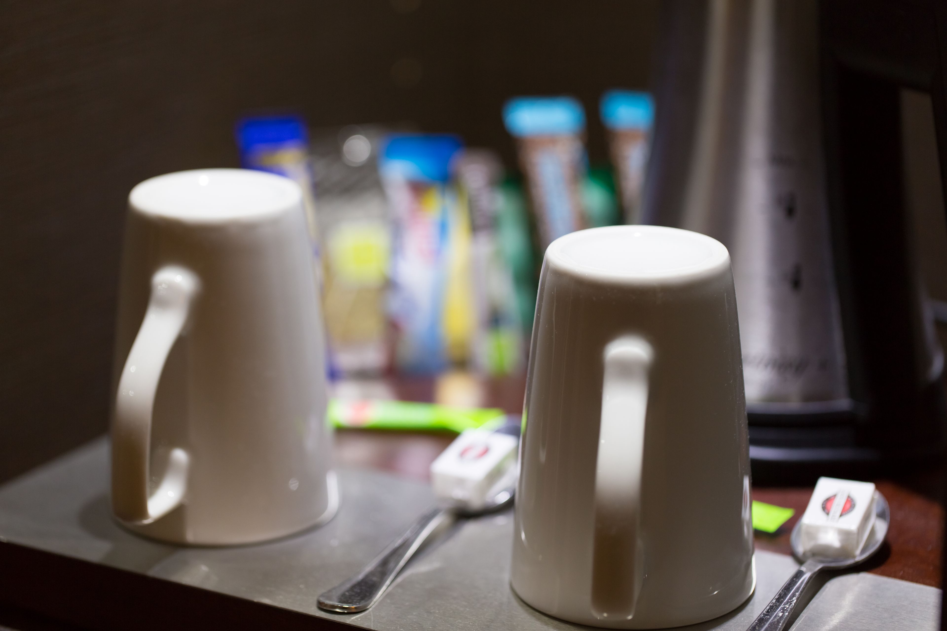 Two white ceramic mugs on a tray with a spoon and a small container, likely a tea bag, in a dimly lit setting.