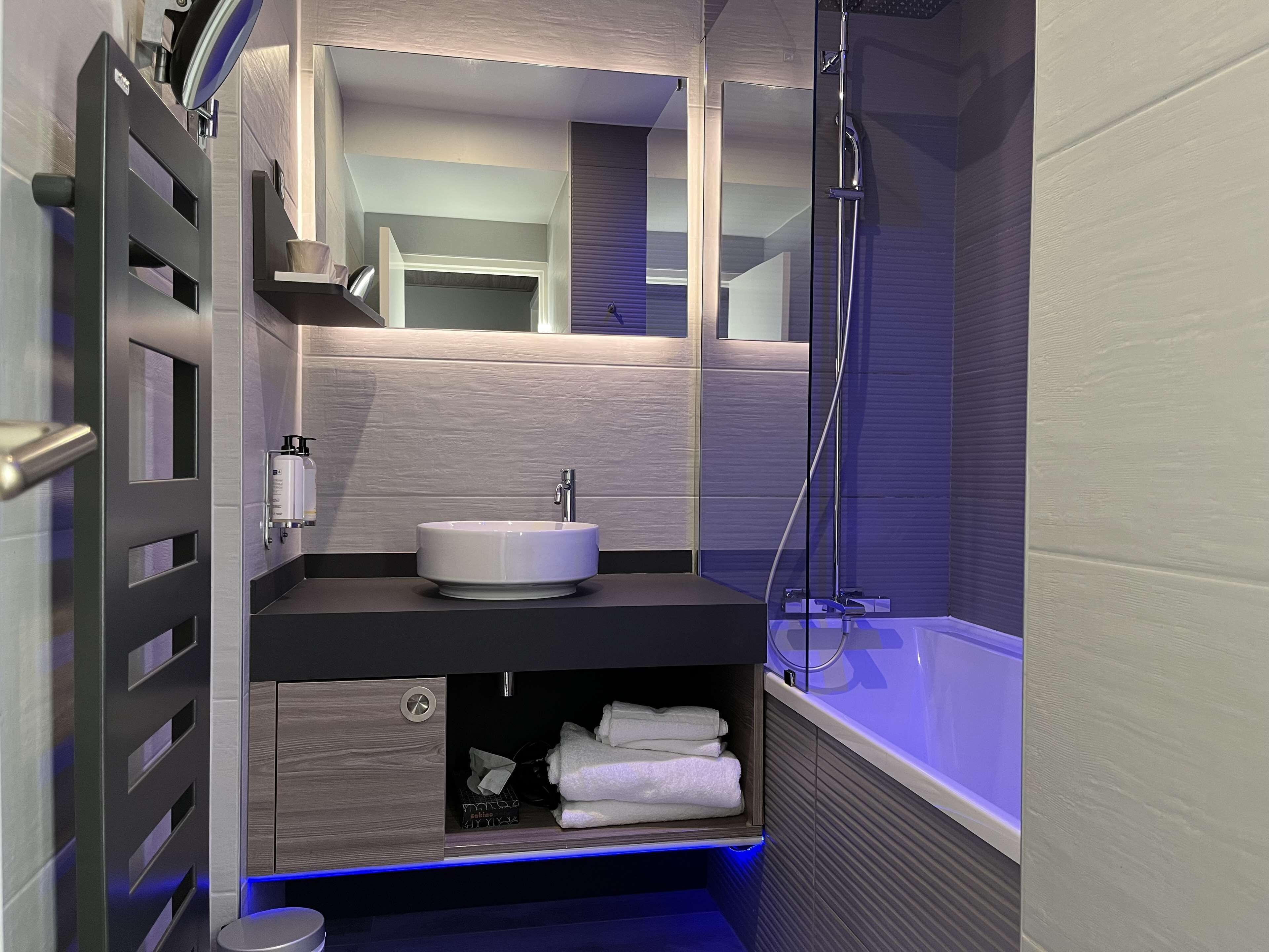 A modern bathroom with a built-in sink, a mirror, a shower, and a towel rack.