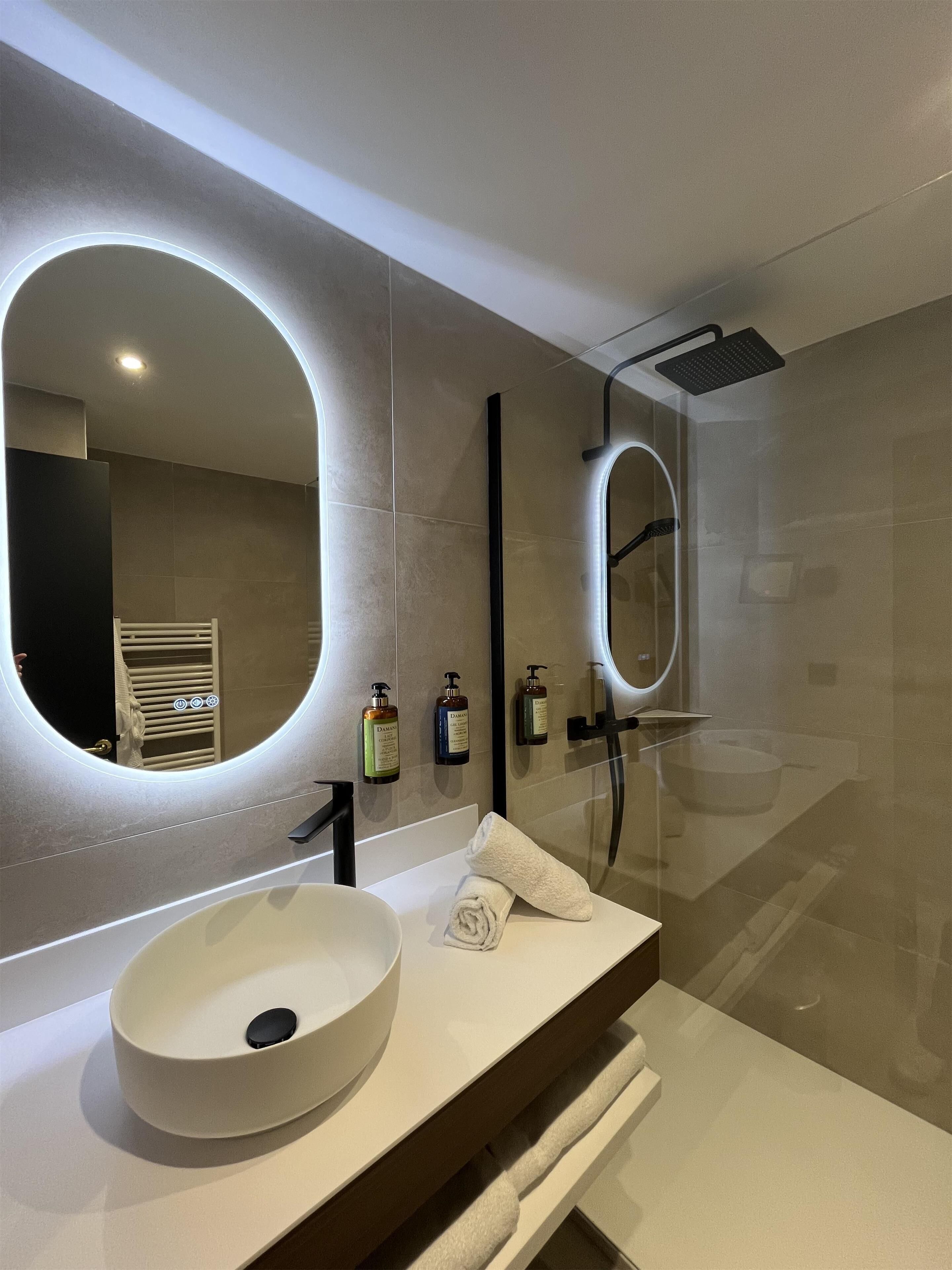 A modern bathroom with a round sink, a large mirror, and a glass-enclosed shower.