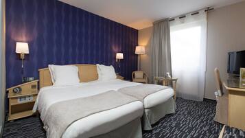 Een hotelkamer met twee bedden, een bureau, een stoel, een televisie en een raam met gordijnen.