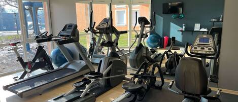 A gym with various exercise equipment, large windows, and a view of the outside.
