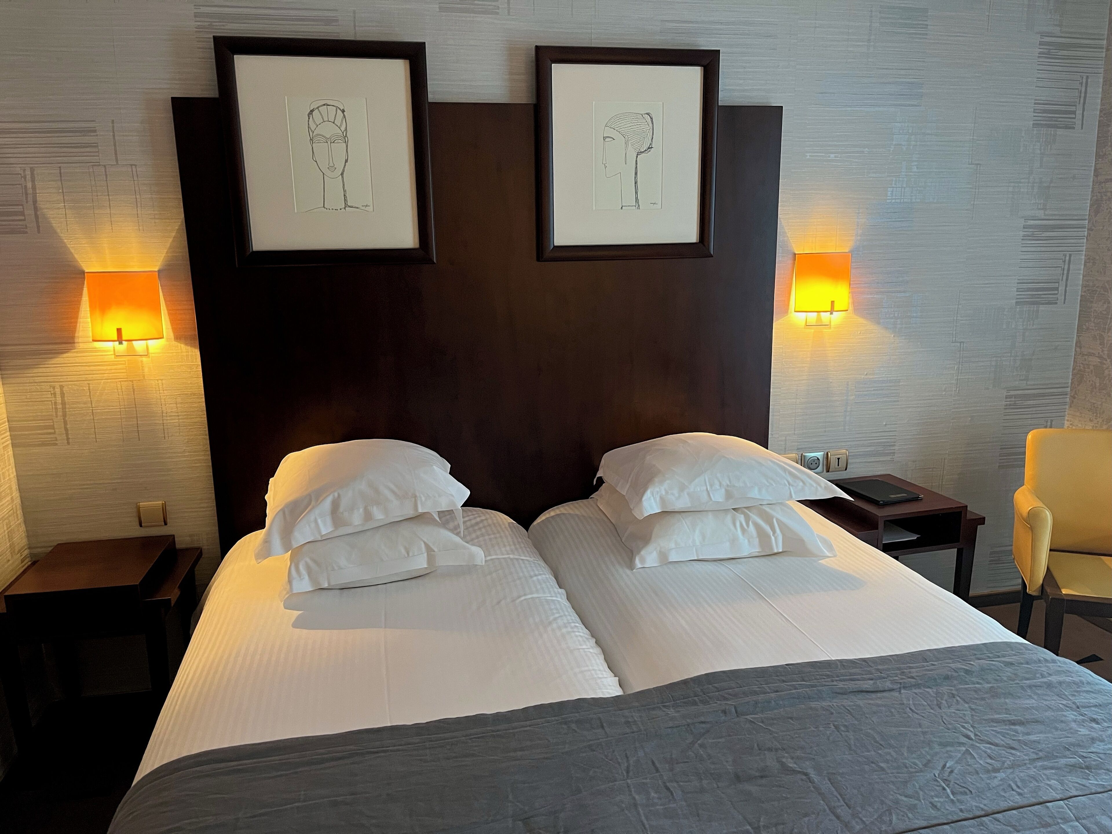 A hotel room with a large bed, two bedside tables, a chair, and two wall-mounted lamps.