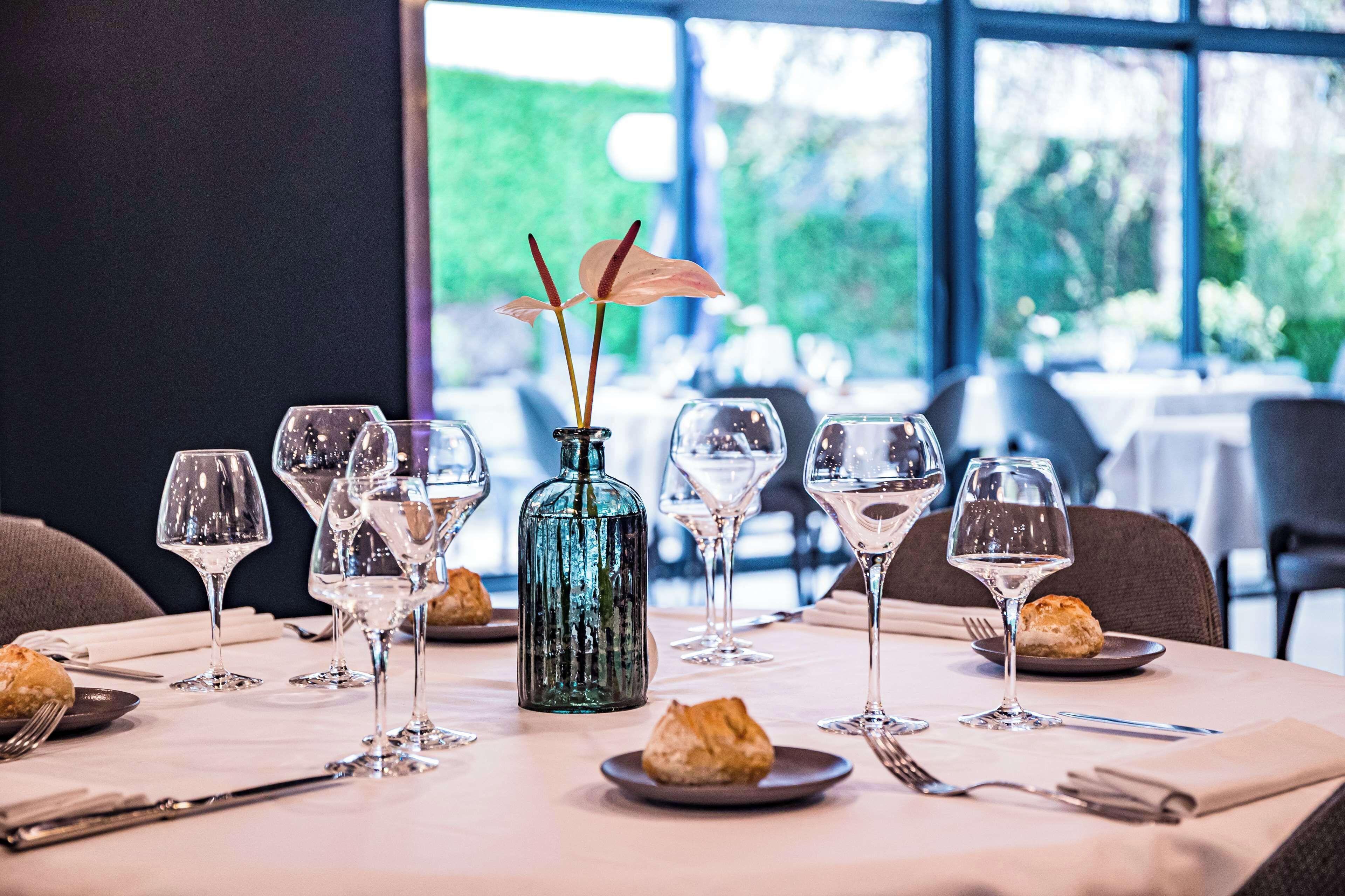 Una mesa de comedor con copas de vino, un florero con flores y platos con pasteles.