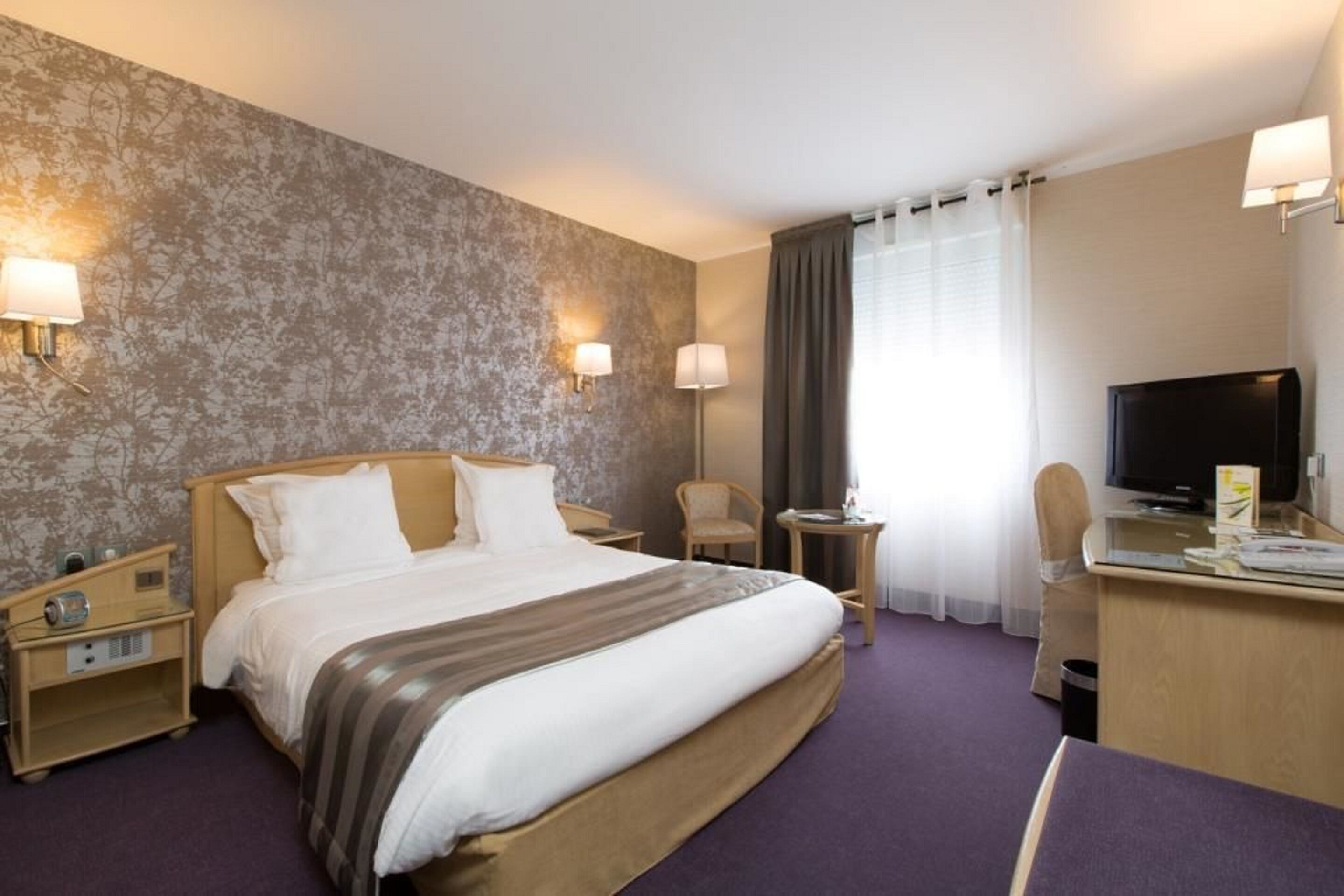 A hotel room with a large bed, bedside lamps, a desk with a television, and a chair.