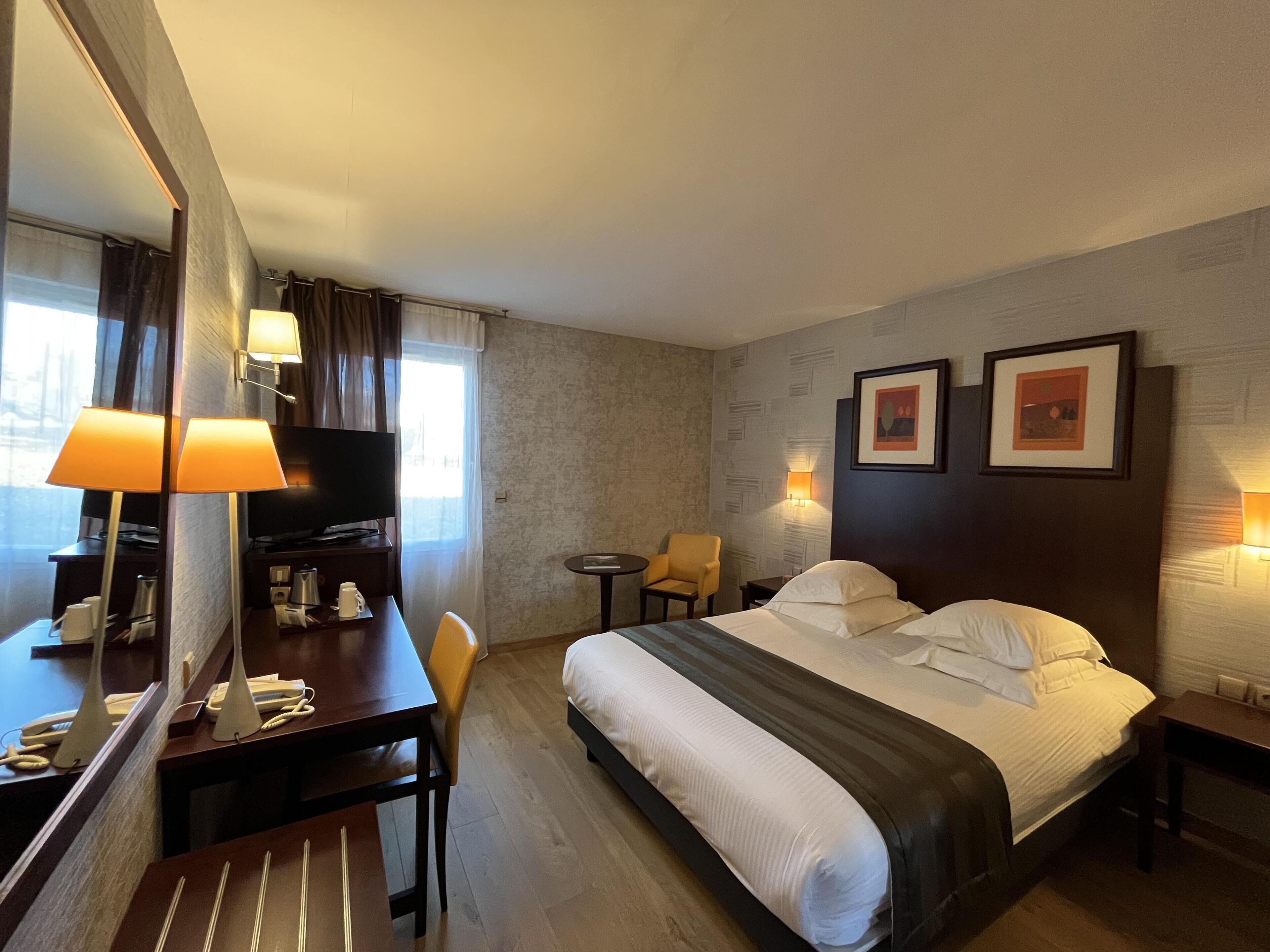 A hotel room with a bed, a desk with a chair, a television, and a small table.