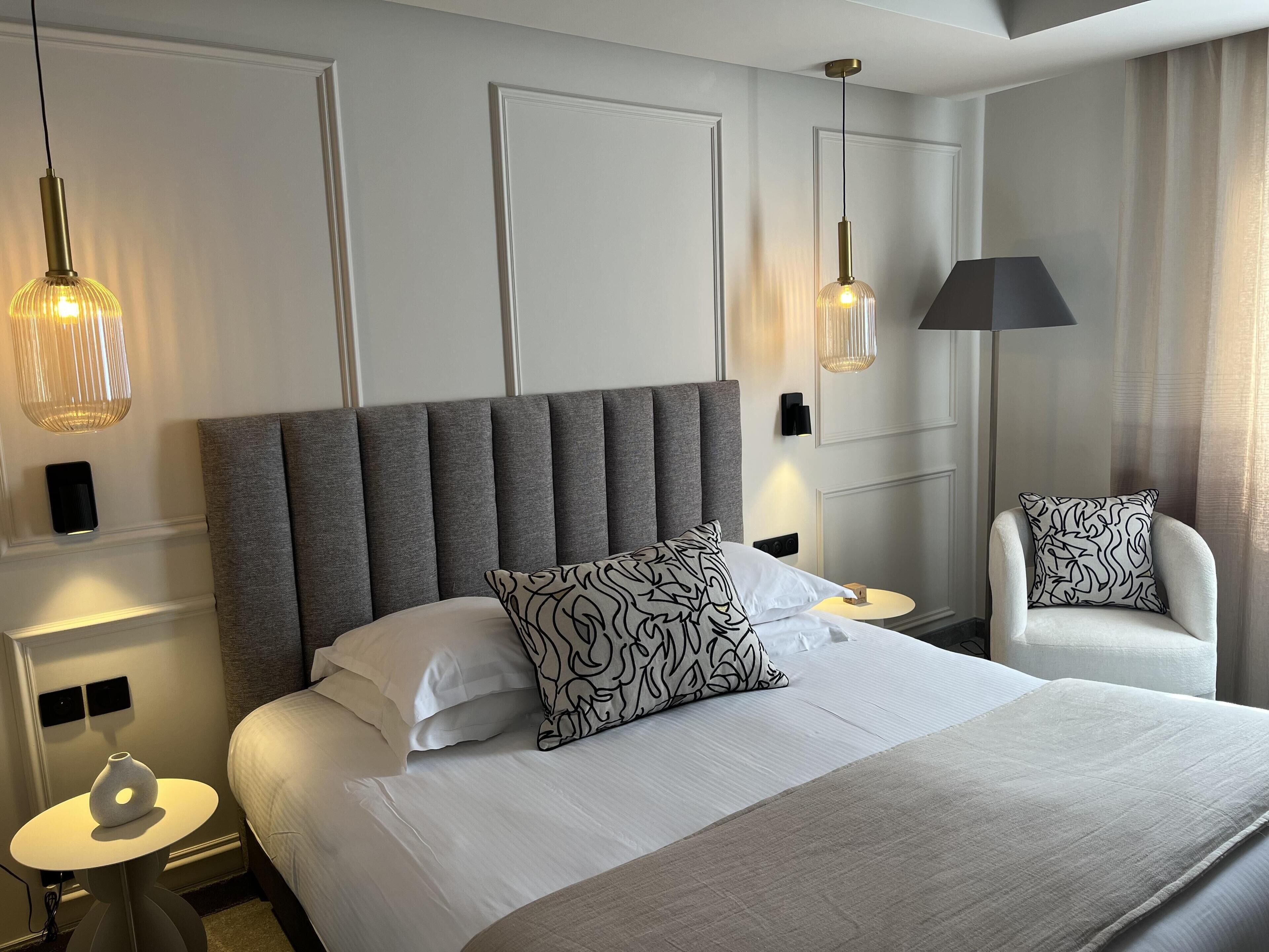 A hotel room with a large bed, two bedside tables, a chair, and pendant lights.