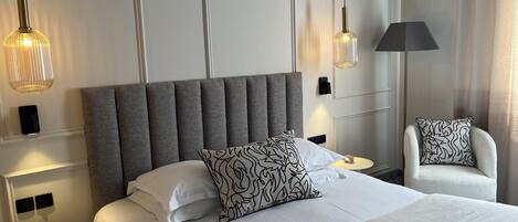 A hotel room with a large bed, two bedside tables, a chair, and pendant lights.