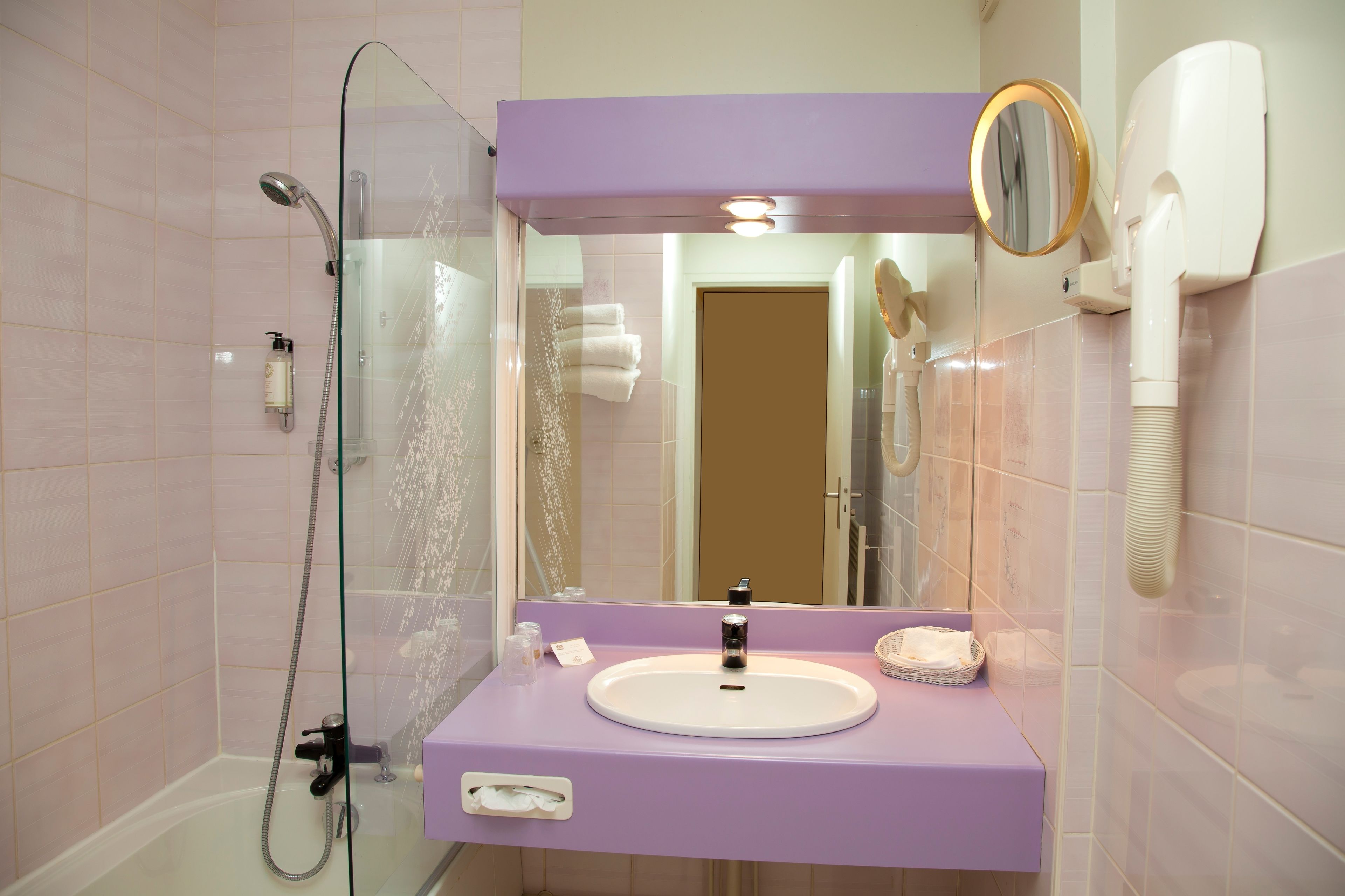 Un baño con ducha de vidrio, lavabo con tocador y secador de pelo montado en la pared.