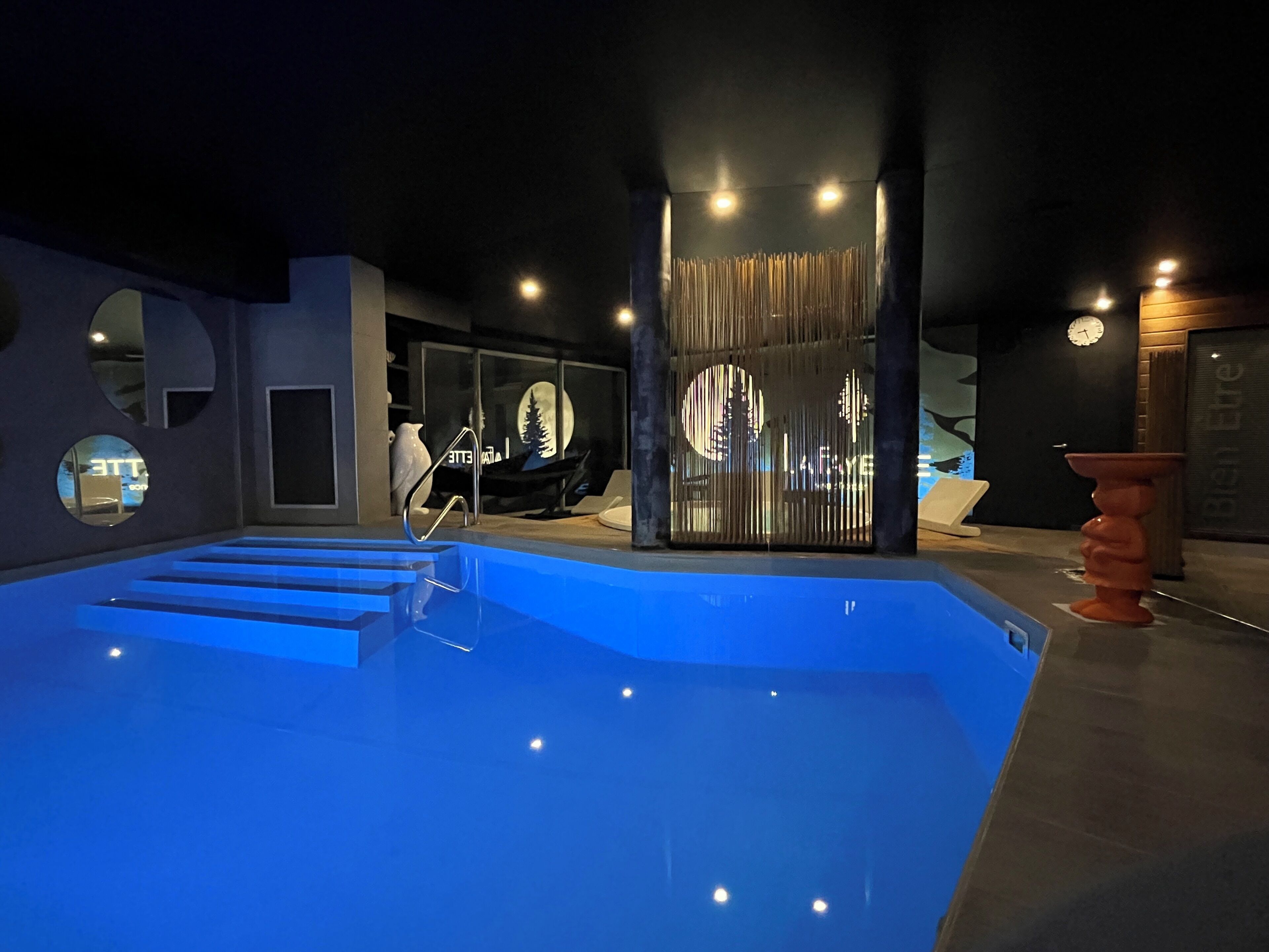 A swimming pool with steps leading into it, a modern interior design with circular windows, and a decorative wall with vertical elements.