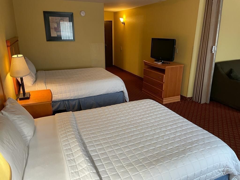 A hotel room with two beds, a television, a dresser, and a lamp.
