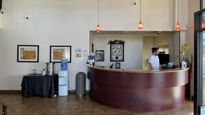 A reception area with a curved reception desk, framed artwork on the walls, a water dispenser, and a trash bin. - Hutchi Bell (Hutchinson)