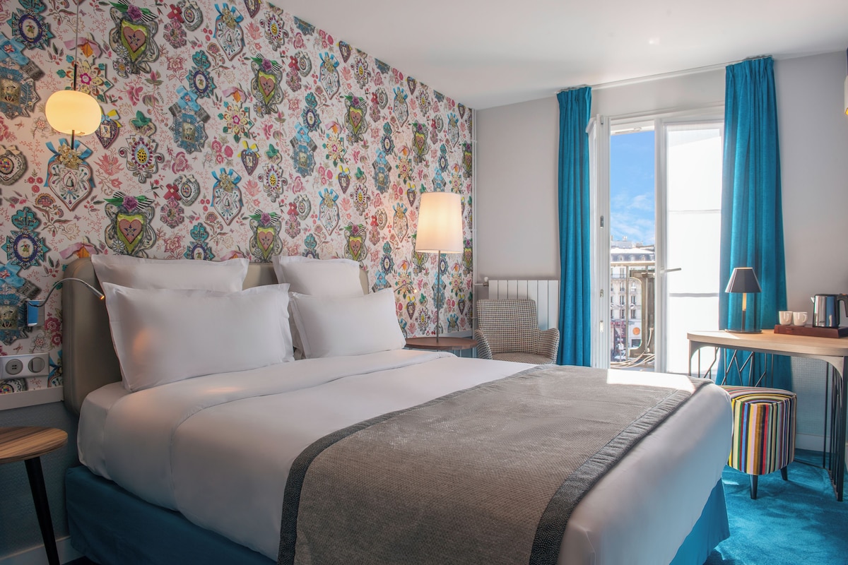 Une chambre d’hôtel avec un grand lit, un bureau, une chaise et une vue sur l’extérieur.