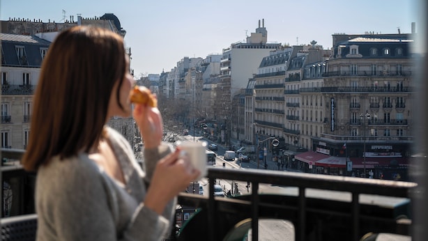 Una persona en un balcón con vistas a un paisaje urbano con edificios históricos y una calle concurrida.