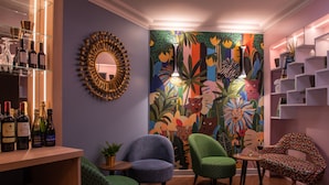 Una habitación con zona de bar, dos sillones, una silla estampada, un espejo y un mural colorido.