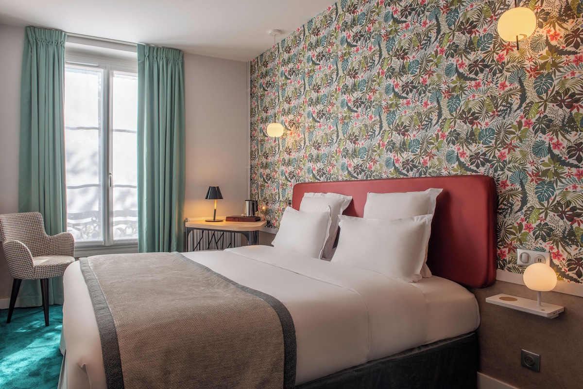 Une chambre d’hôtel avec un grand lit, une chaise, un bureau et une fenêtre avec des rideaux.