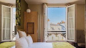 Habitación de hotel con cama, armario de madera, vista a edificios por la ventana y una silla.