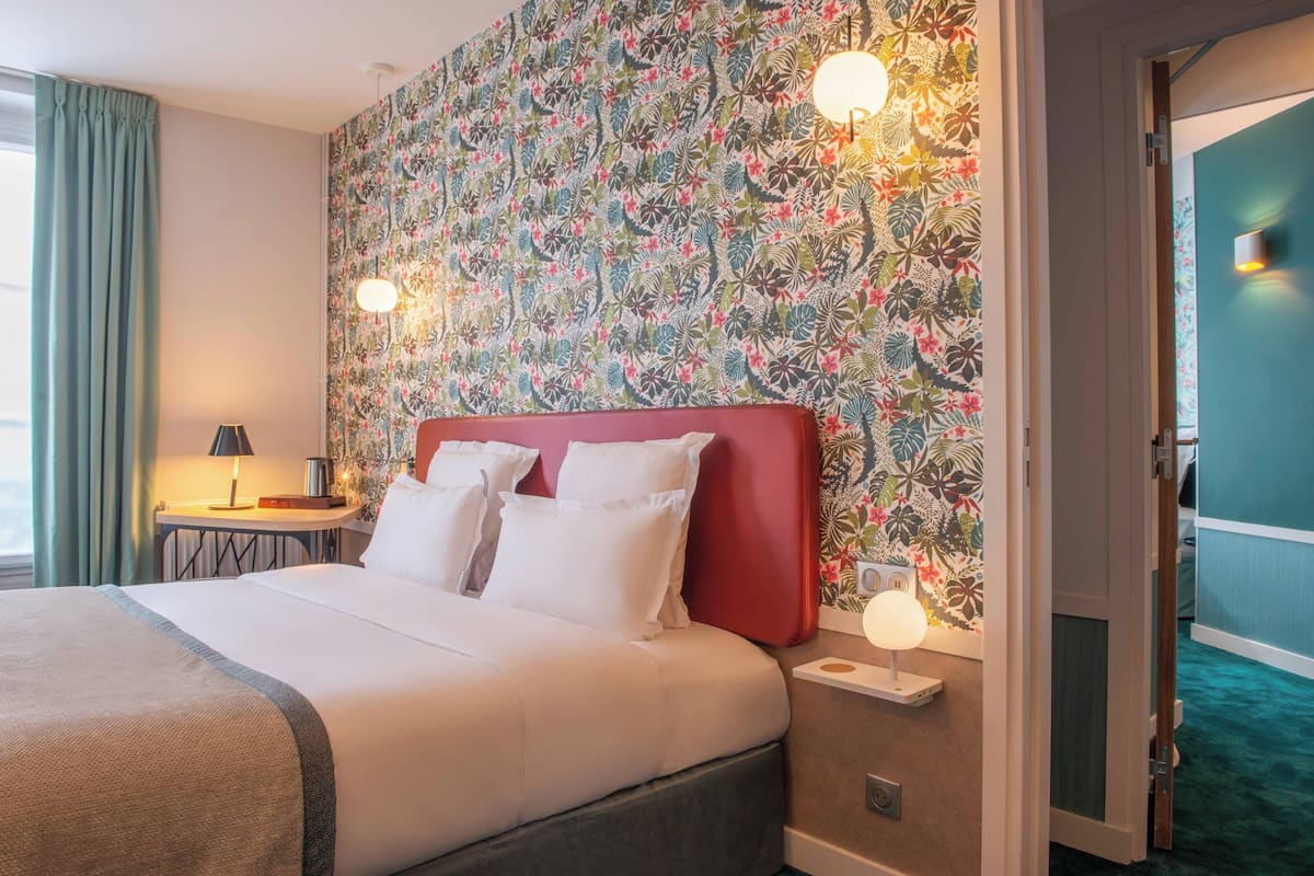 A hotel room with a bed, a nightstand, a lamp, and a floral wallpaper.