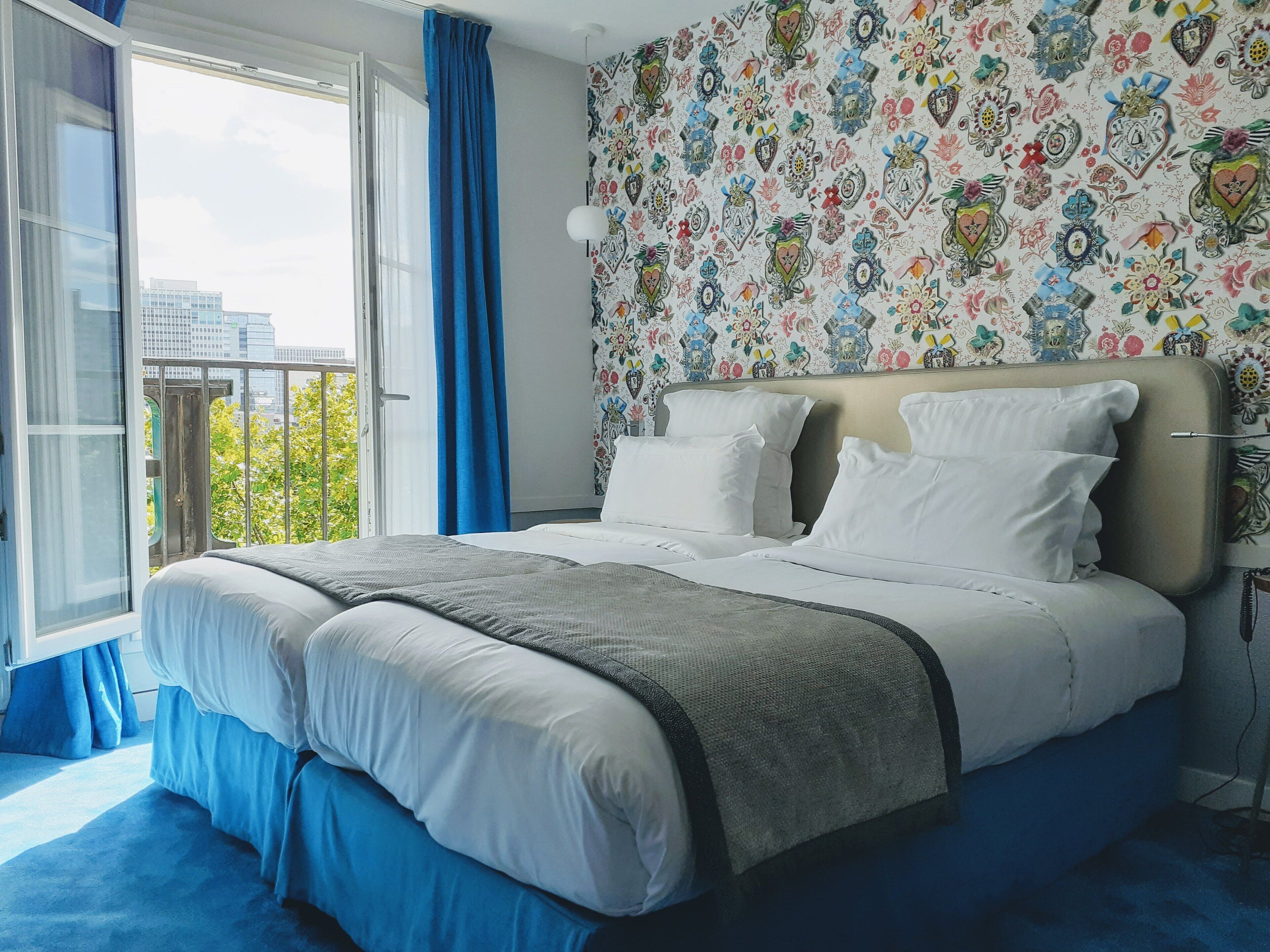 Un dormitorio con una cama grande, vistas de la ciudad desde un balcón y un papel tapiz estampado.