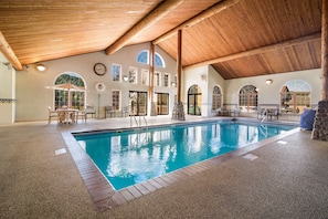 An indoor swimming pool with a wooden ceiling, stone pillars, and arched windows.