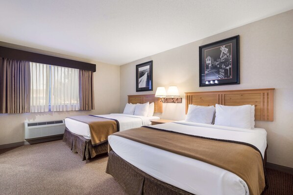 A hotel room with two beds, a large window with curtains, a wall-mounted picture, and a wooden headboard.
