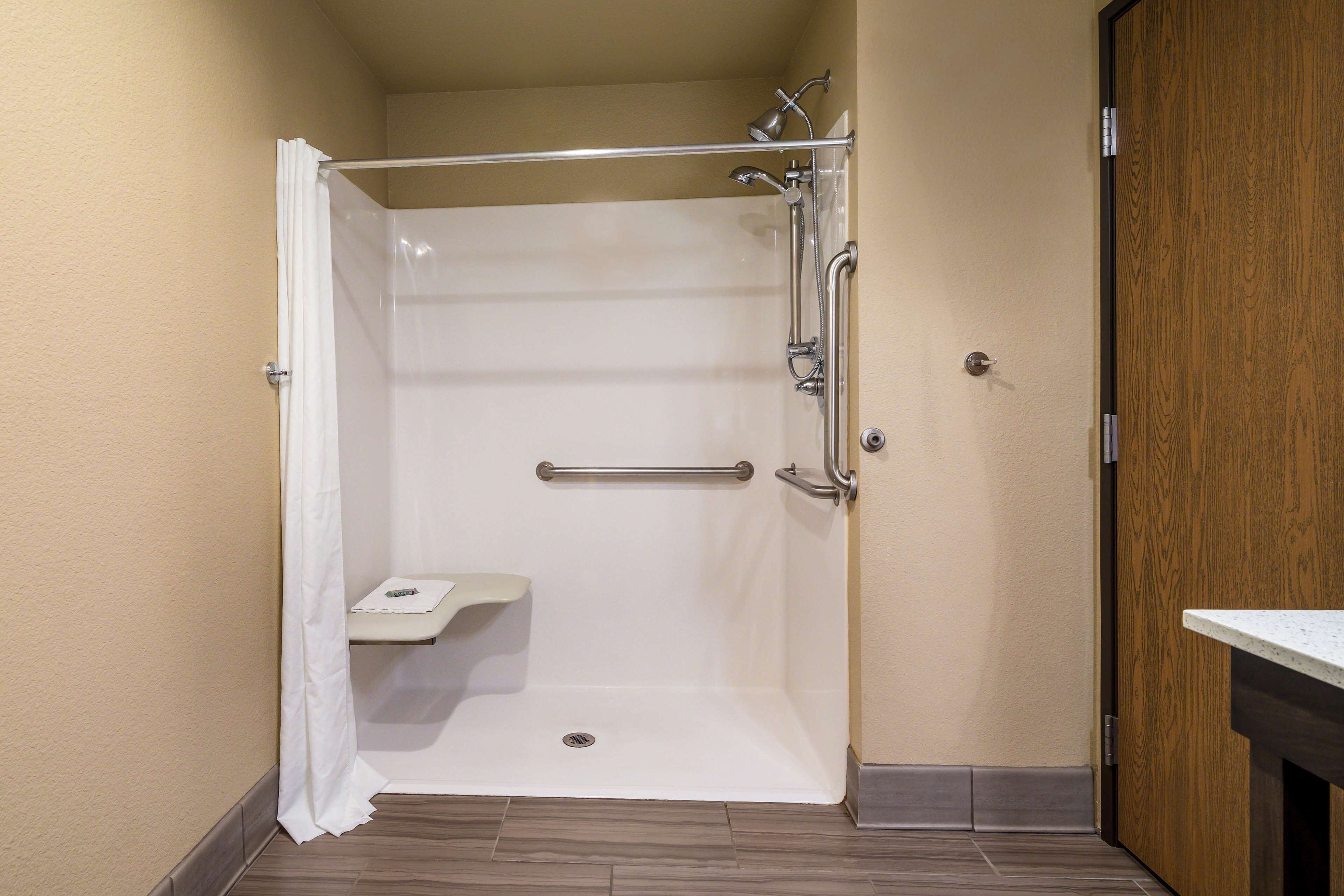 A walk-in shower with a grab bar, a small shelf, and a wooden door.